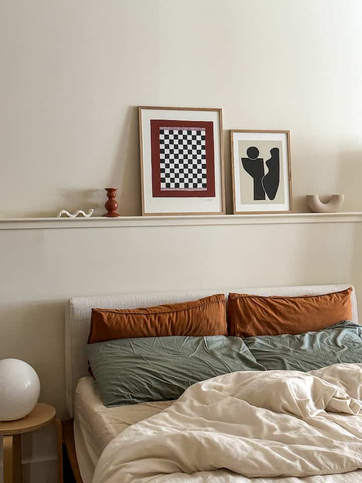 Beige and brown toned bedroom featuring a bed centered with a nightstand and two framed artworks on the wall, creating a cozy atmosphere