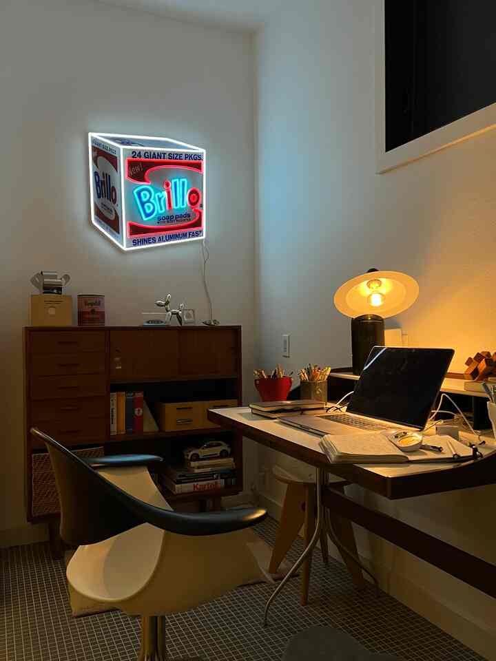 Warmly lit mid-century modern style home office featuring a wooden desk, armchair, and Brillo box wall decor