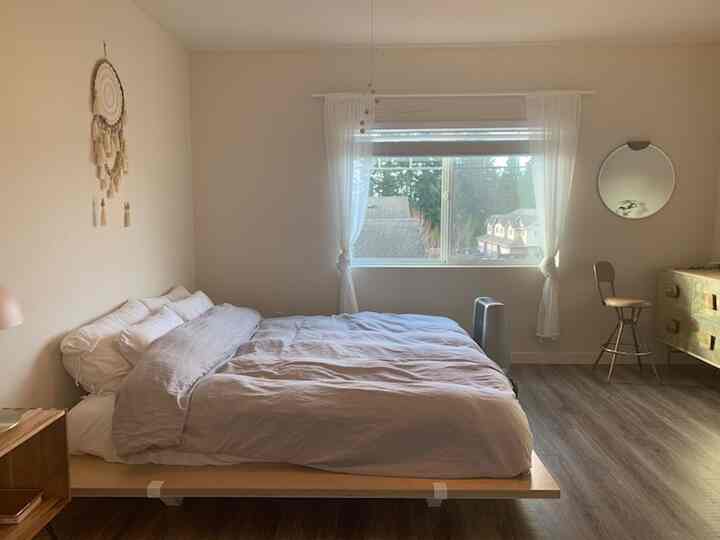 White and beige toned bedroom featuring simple mid-century modern furniture and natural wood flooring creating a calm atmosphere