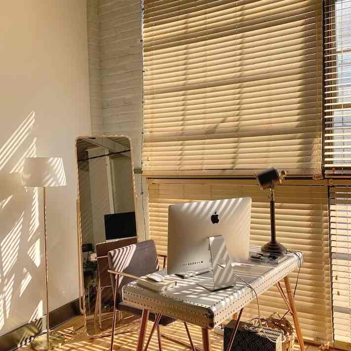 Warm wood tones and beige home office space featuring angled desk by window with full-length mirror, cozy interior filled with sunlight