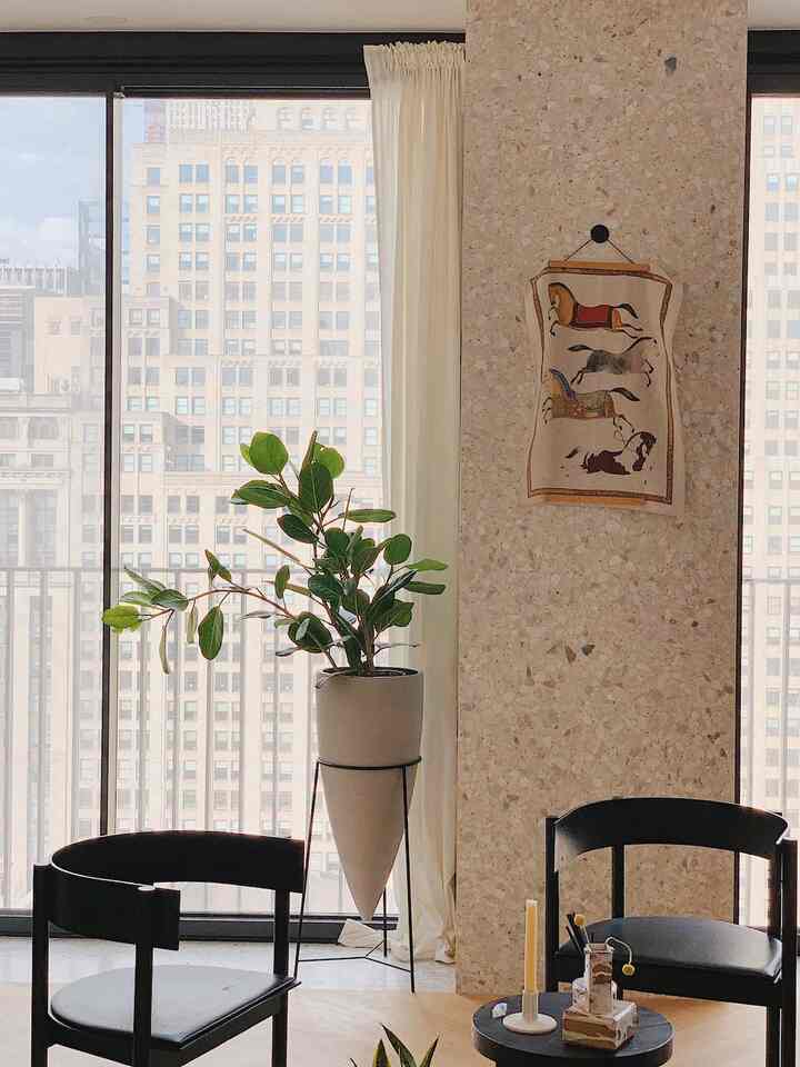 Bright natural living room with large windows, white curtains, stone wall, and green plant creating a harmonious space
