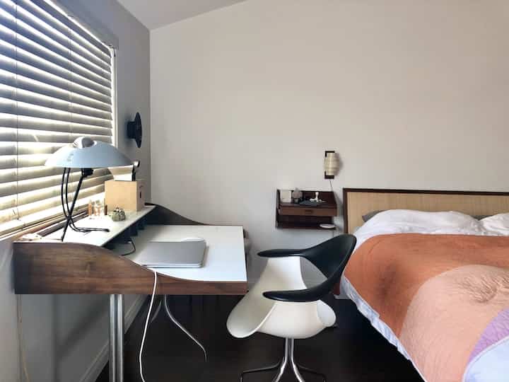 White-walled bedroom with brown wood-tone furniture for single household, featuring a desk and bed in a vintage style setting