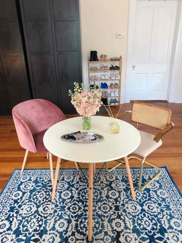White and wood tone dining room featuring a round dining table with two distinct chairs, floral centerpiece, and organized shoe rack creating a neat atmosphere