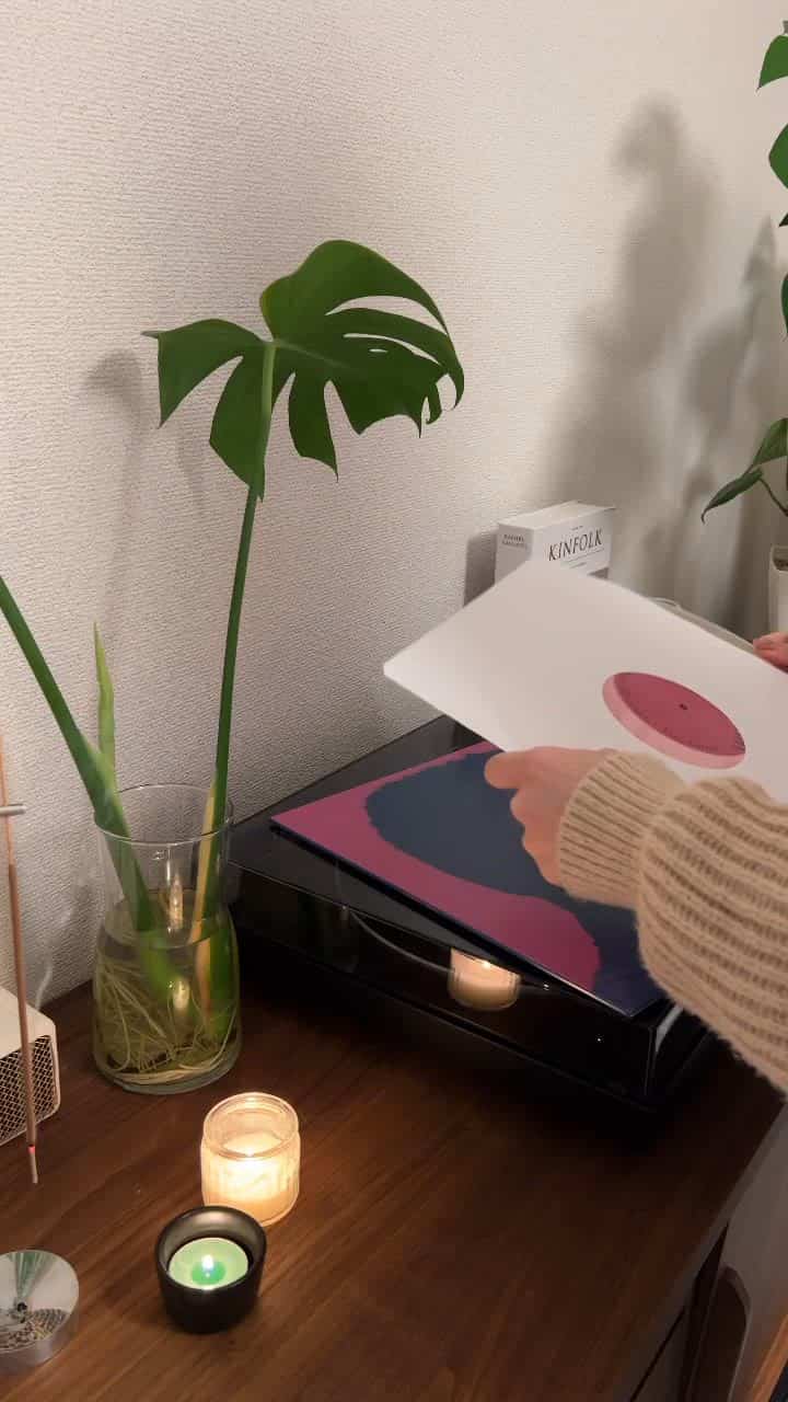 A calm living room interior with dominant pink tones, featuring a Bluetooth turntable, plants, and lit candles
