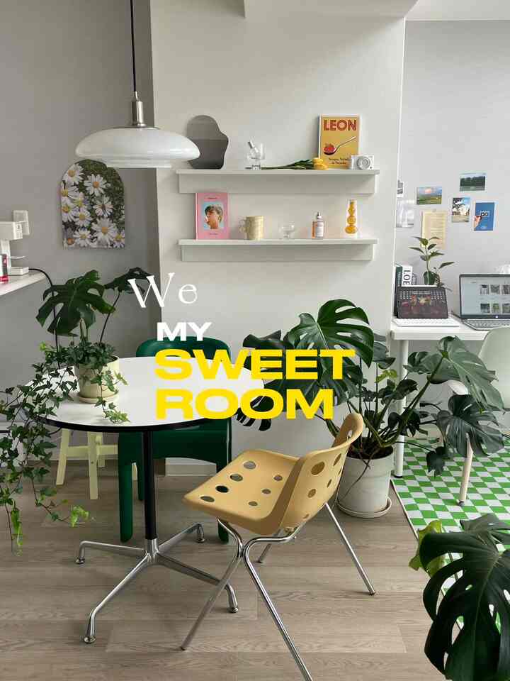 A simple studio apartment with white and green tones, featuring a dining table, plants, and a cozy home office setup