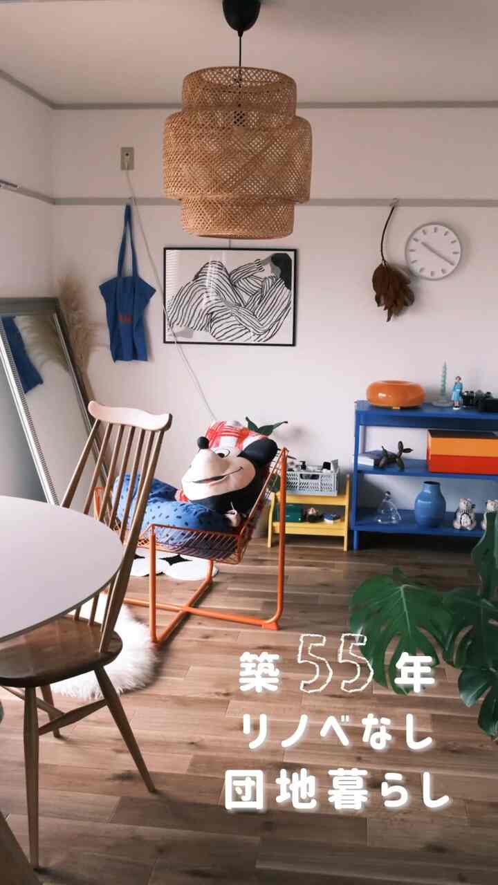 Living room with wood-tone flooring and blue shelving, featuring a rattan pendant lamp and orange frame chair creating a cozy atmosphere