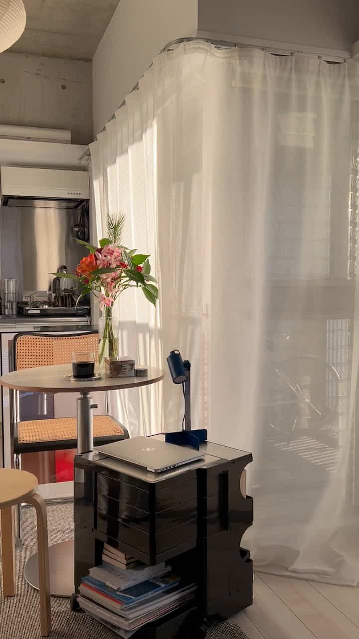A white and natural toned studio apartment featuring sheer lace curtains and warm natural light creating a cozy atmosphere