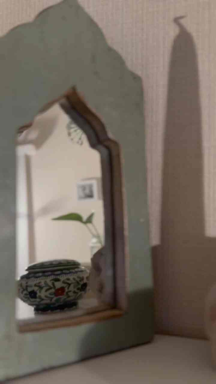 ベージュの壁とナチュラルな鏡が配置されたリビング、花瓶と植物が印象的な空間