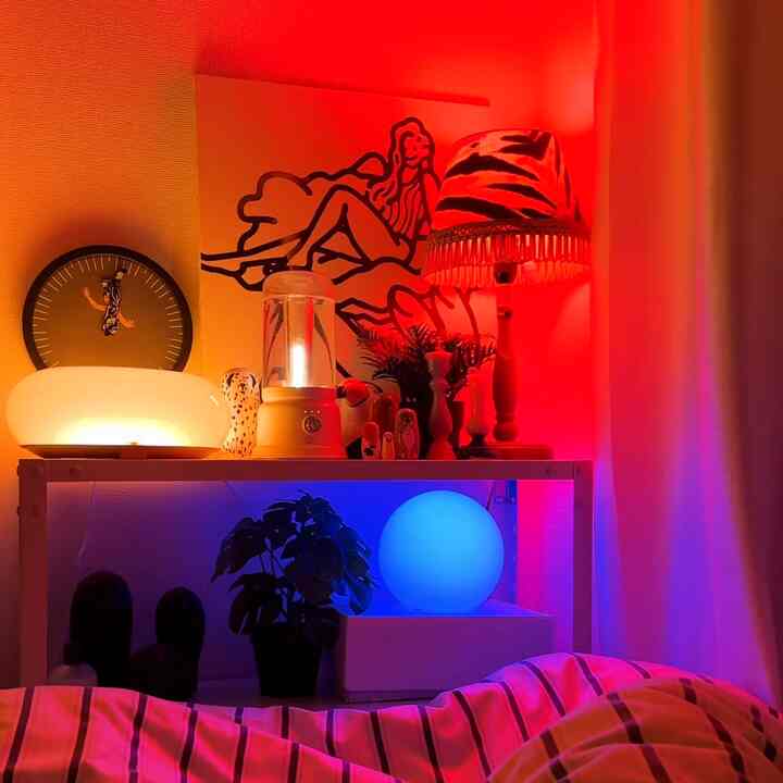 Studio apartment interior with red and blue mood lighting, featuring table lamps and plants creating a cozy atmosphere