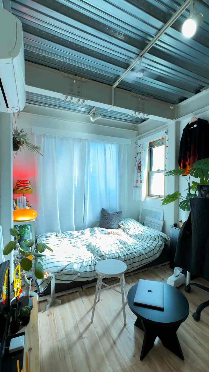 白とナチュラルカラーのモノトーンが基調のワンルーム、一人暮らし向けの整ったベッドとデスクが配置された印象的な空間