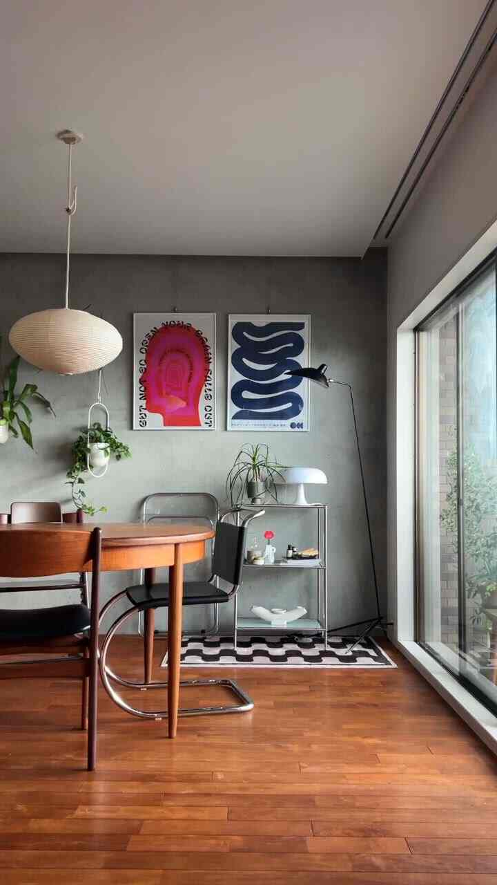 グレーのコンクリート壁と木目調の床が調和したモダンダイニング、抽象的なポスターとフロアランプが配置された雰囲気のあるインテリア