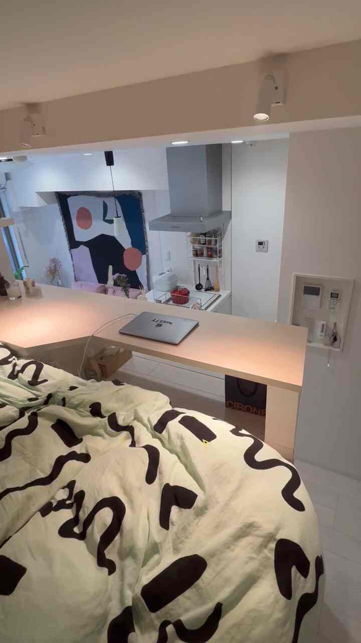 Natural-toned studio bedroom with mint and black patterned duvet cover showcasing a compact space including a small home office desk