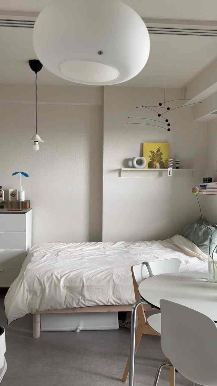 Simple natural studio bedroom with white base and yellow accent, featuring bed, wall shelf, and round desk arranged in a modern layout