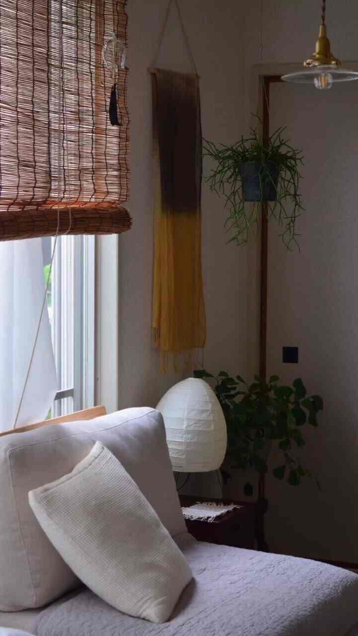 Natural tone living room featuring white sofa and cushion, bamboo blinds, plants, and floor lamp in cozy atmosphere