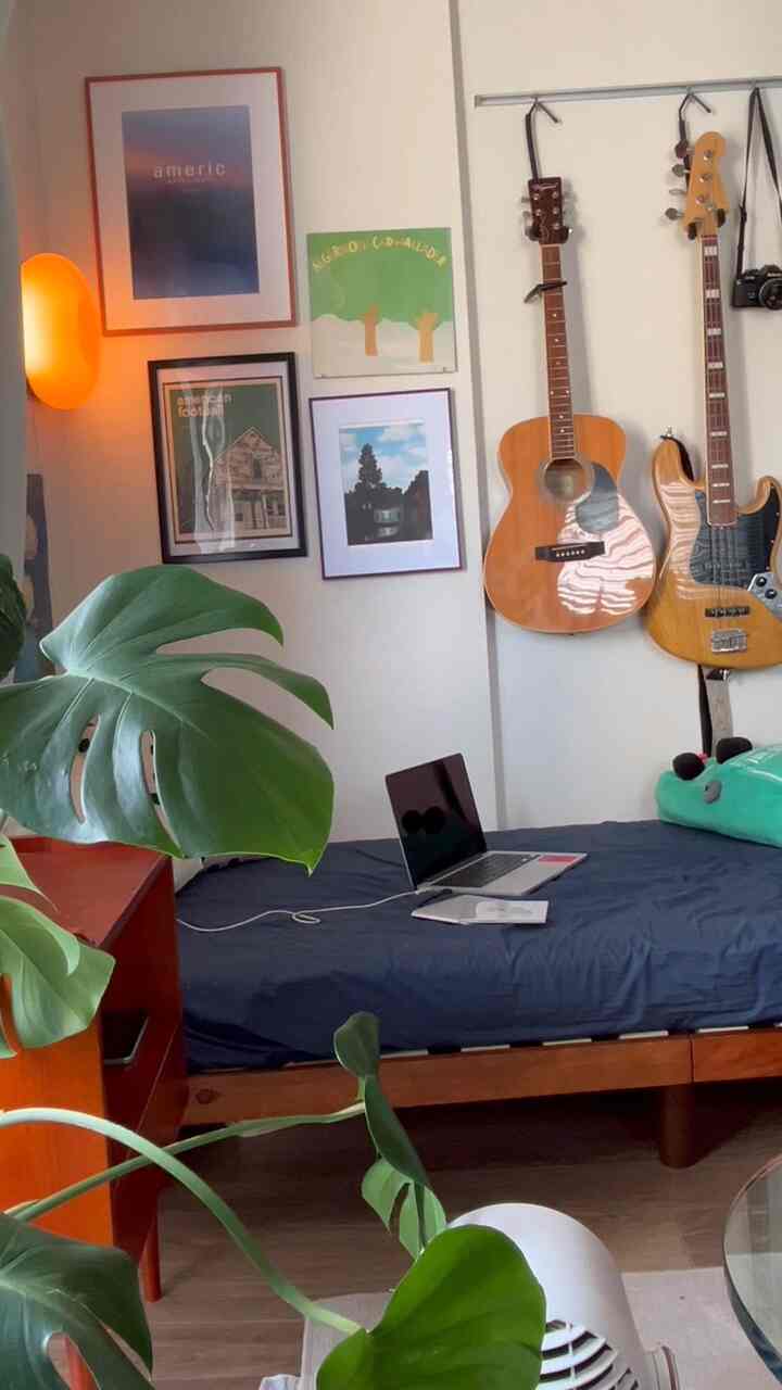 ブラウンの木製家具と緑の植物が調和する8畳のワンルーム寝室、間接照明とウォールアートがモダンな雰囲気を演出