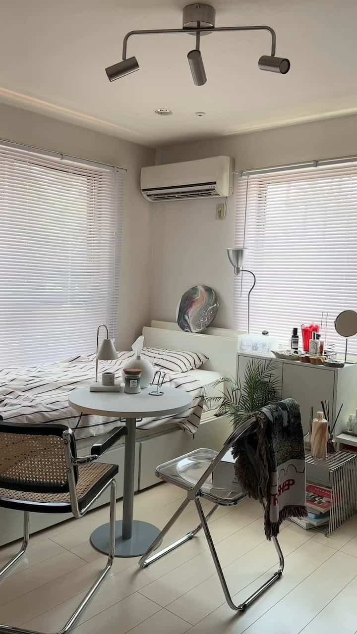 白を基調としたナチュラル素材の8畳寝室、ベッドと丸テーブル、椅子が配置されたモダンで清潔感のあるインテリア