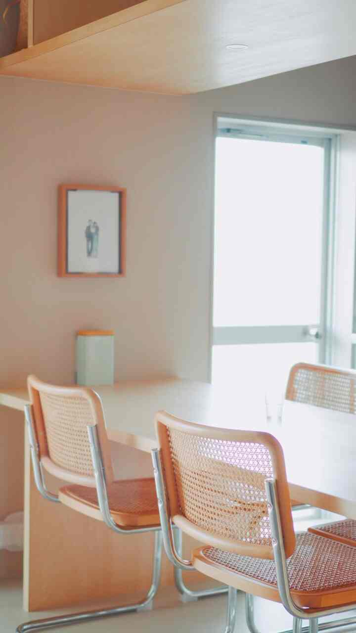 明るいナチュラルカラーと木目調のシンプルなリビング、ラタンのダイニングチェアと額縁が配置された空間