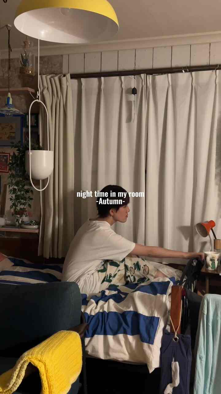 白いカーテンと青いストライプの掛け布団がある寝室、黄色のペンダントライトとソファが配置された雰囲気のある空間