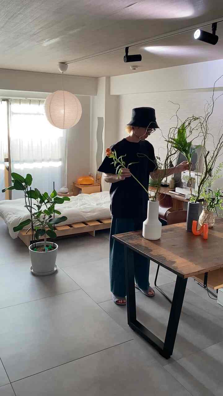 白い壁と木目調の家具が調和したワンルーム、中央に花瓶と植物の置かれたシンプルで自然な雰囲気のインテリア