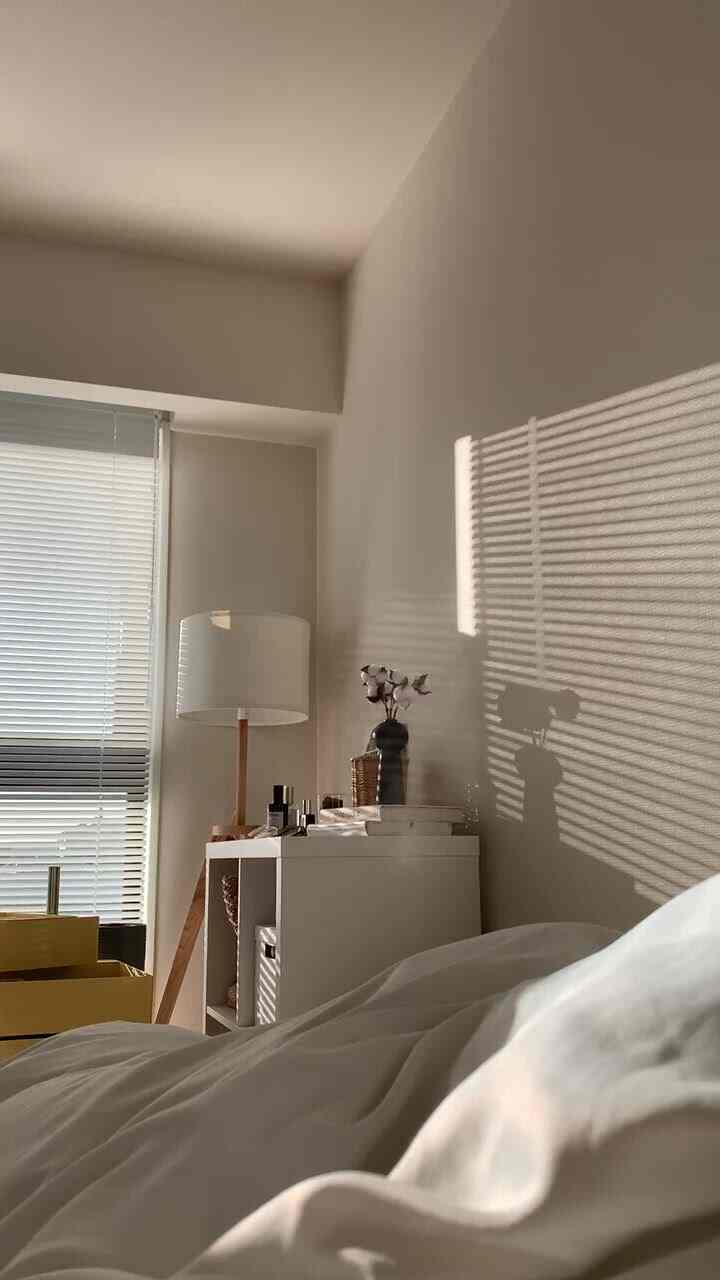 ホワイトとナチュラルカラーの寝室、ブラインドの影が壁に映る穏やかな朝のインテリア