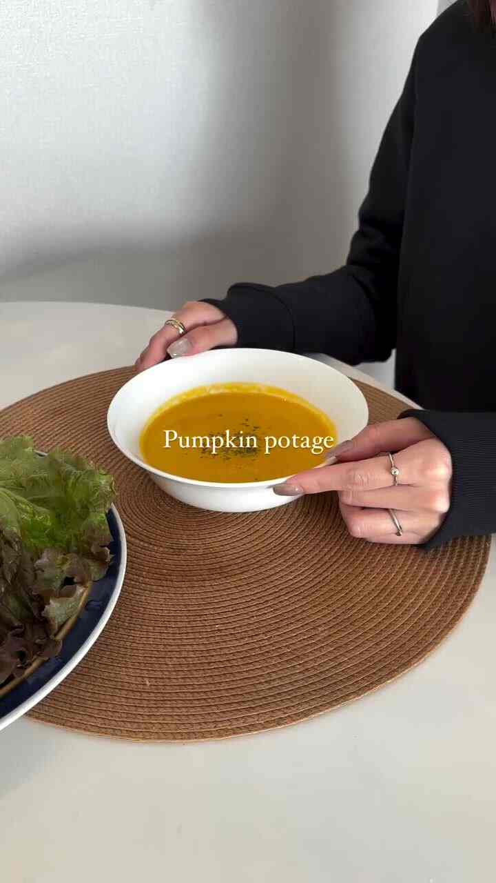 ナチュラルな色調のダイニングスペース、丸いランチョンマットの上にオレンジ色のかぼちゃスープと新鮮なサラダが置かれた雰囲気のあるおうちカフェインテリア