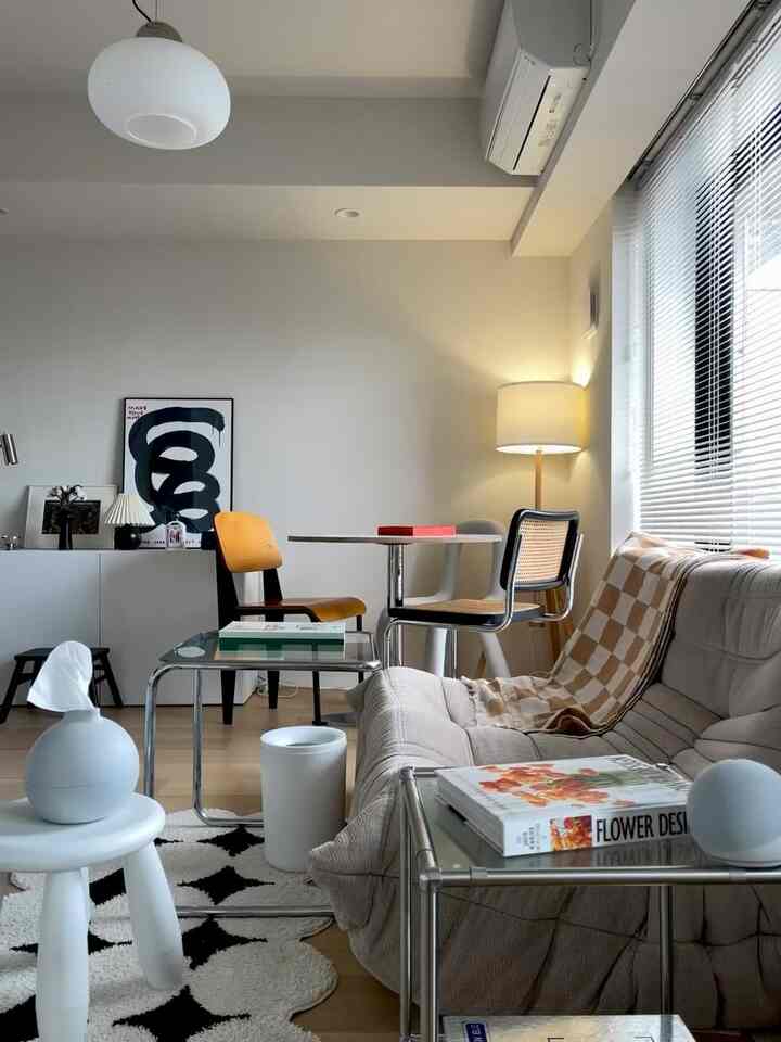 Natural modern 2-person living room with white walls, beige sofa, wooden chairs, glass tables, and warm lighting