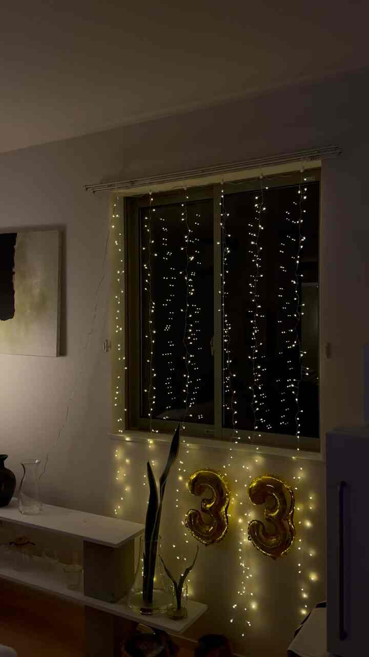 Warm gold and white toned living room featuring string lights around window and golden balloons celebrating 33rd birthday