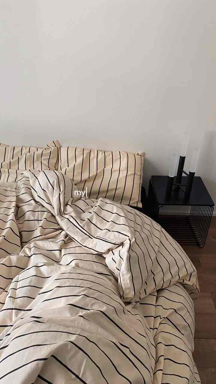 A simple and modern bedroom featuring beige and black striped bed linen with a black side table