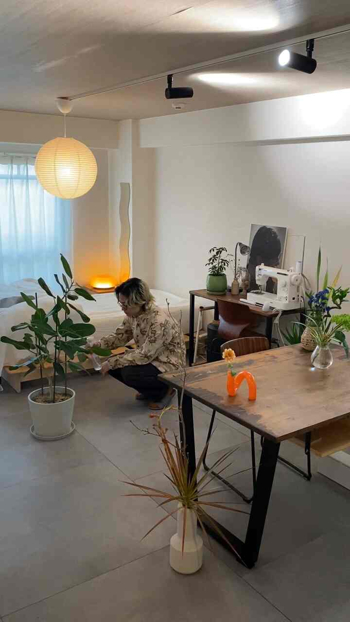 Natural-toned studio apartment featuring solid wood furniture and multiple plants with a cozy, calm atmosphere