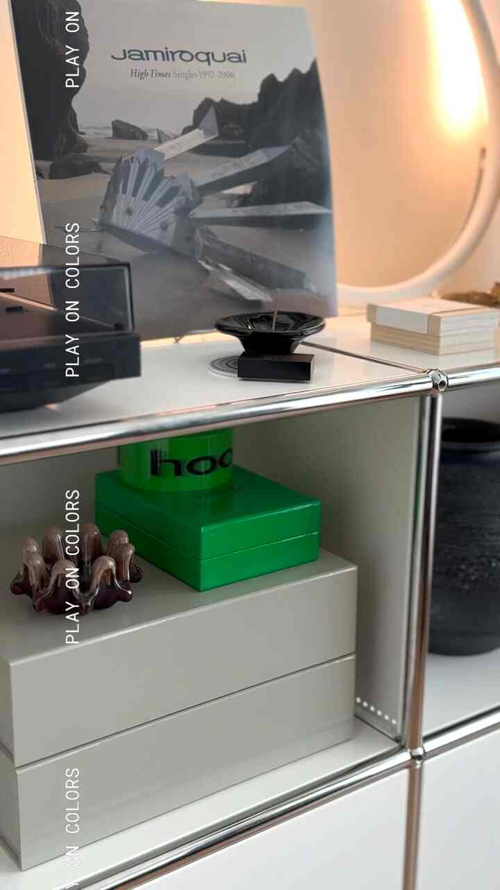 シルバーメタルフレームとホワイトシェルフのミニマルなキャビネット、グリーンの箱とオブジェが配置された清潔感のあるインテリア