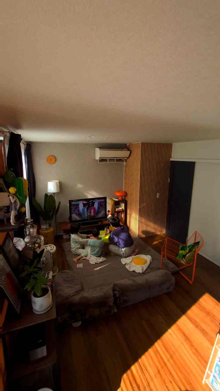 Living room with dark brown wooden floor and natural wood wall paneling, children sitting center watching TV in cozy atmosphere