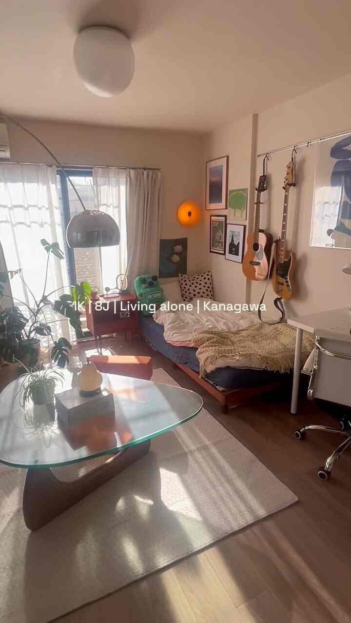 Warm natural-toned 8-tatami studio featuring a bed, glass-top coffee table, leafy plants, and cozy indirect lighting for a single household