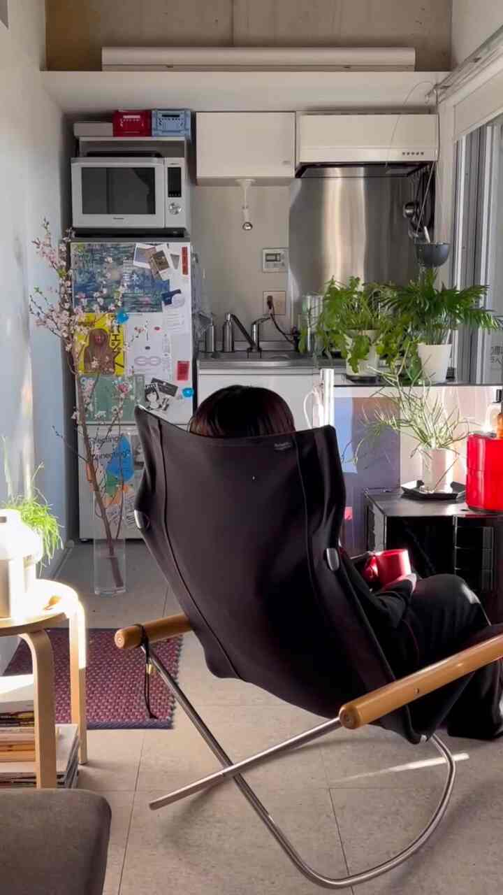 明るいホワイトトーンのワンルームキッチンスペース、黒のロッキングチェアと多様な植物が配置された居心地の良い一人暮らしの空間