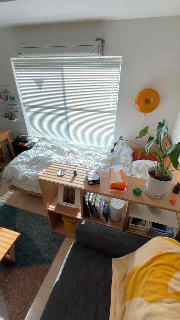 Bright white and natural wood-toned 7-tatami studio featuring bed, sofa, shelves, and a plant creating a cozy atmosphere