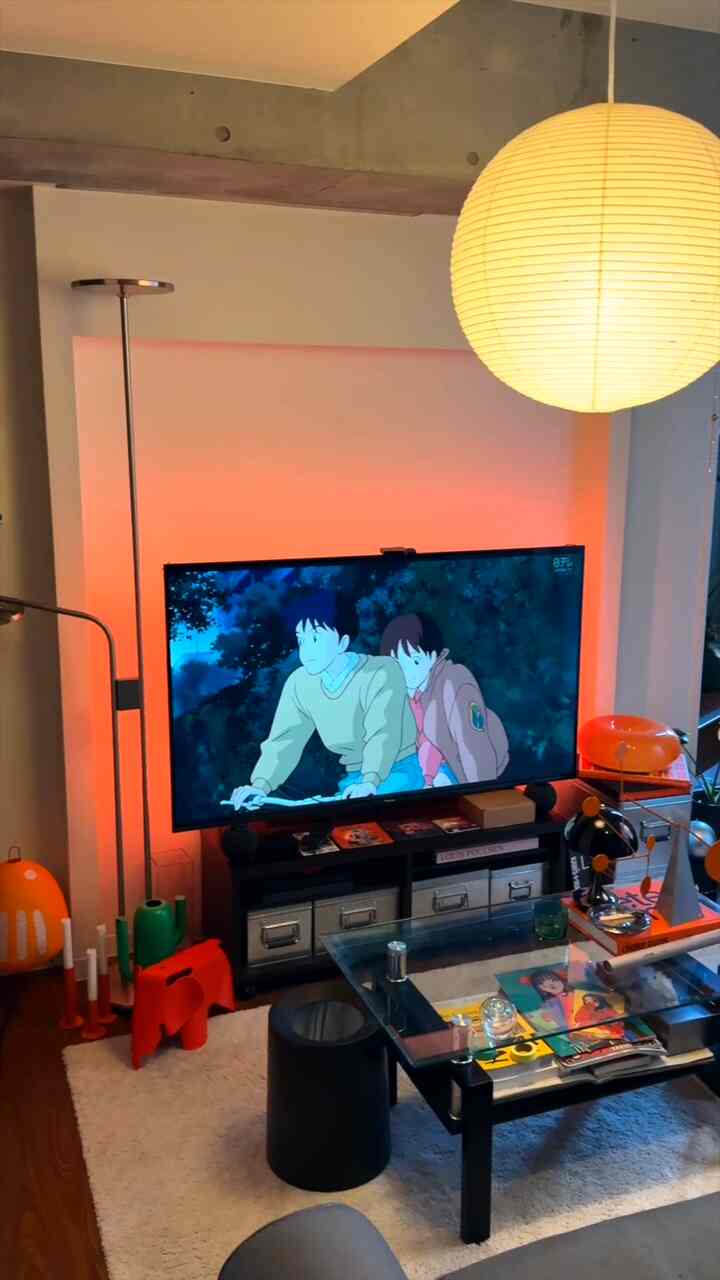 オレンジの照明とペンダントライトが映える、テレビとガラスのコーヒーテーブルが配置されたモダンなミッドセンチュリースタイルのリビング