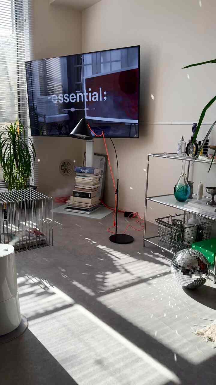 ホワイトトーンの1LDKリビング、壁掛けテレビとメタルシェルフ、読書灯が配置された印象的な空間