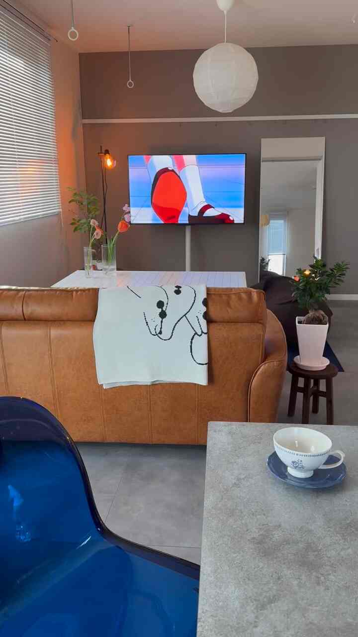 チャコール色の壁とセメントの床が調和するリビング、ブラウンのソファと透明なブルーチェアが置かれたモダンで落ち着いた空間