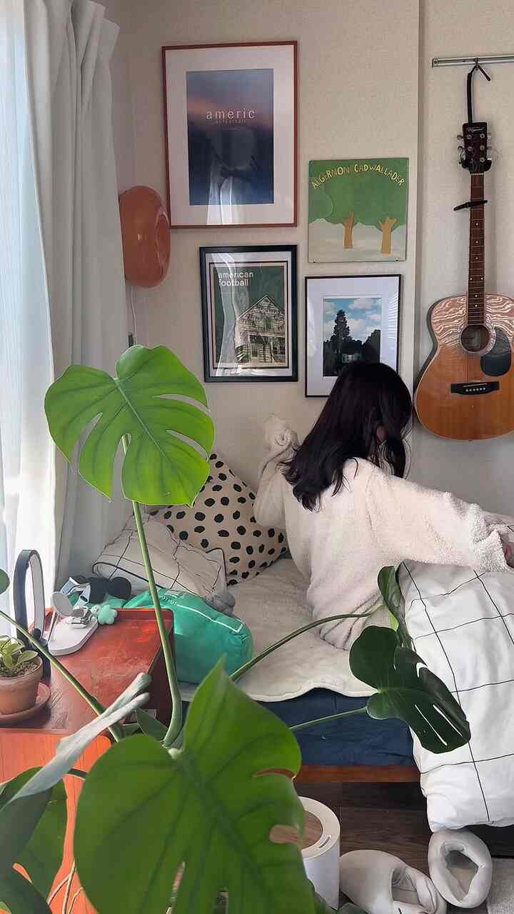 ナチュラルな色調の8畳ワンルーム寝室、観葉植物と額装された壁アートが配置された暖かく居心地の良い空間