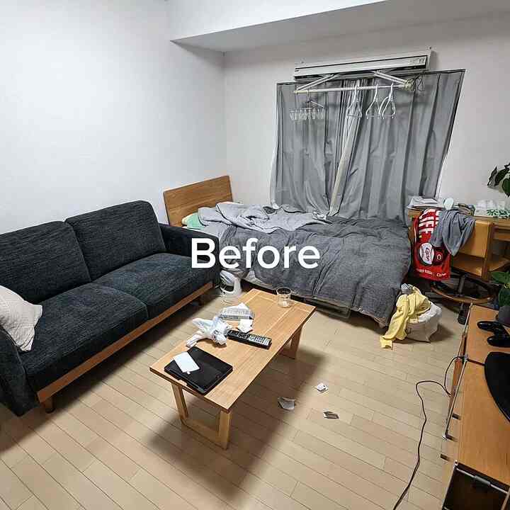 Natural toned 1K space for single household featuring beige flooring, dark gray sofa, and bed arranged compactly