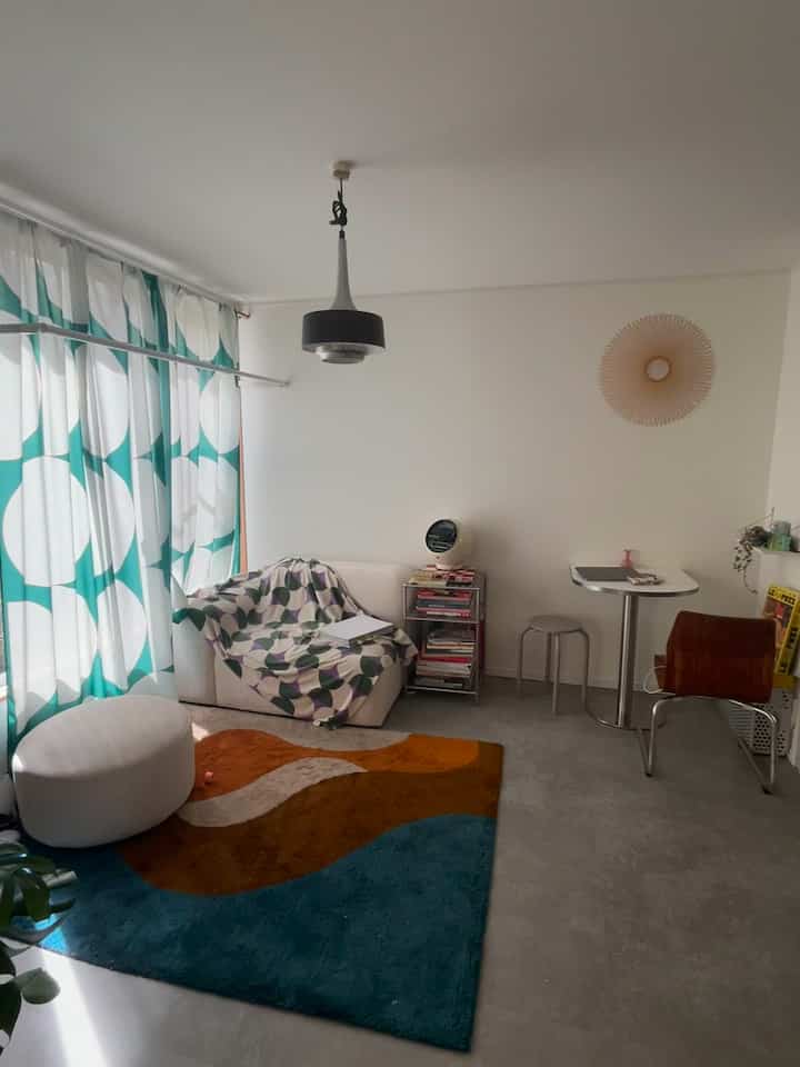 White and green toned 1LDK living room featuring a small sofa, large curtains, and a colorful rug with a cozy ambiance