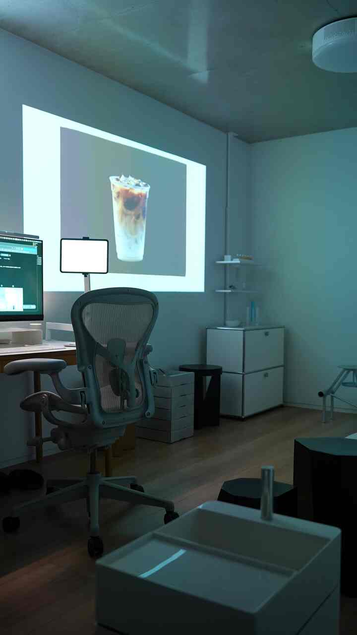 白い壁と木目調の床に囲まれたコンパクトなホームオフィス、オフィスチェアとデスク、コーヒーの映像が映し出された雰囲気のあるインテリア