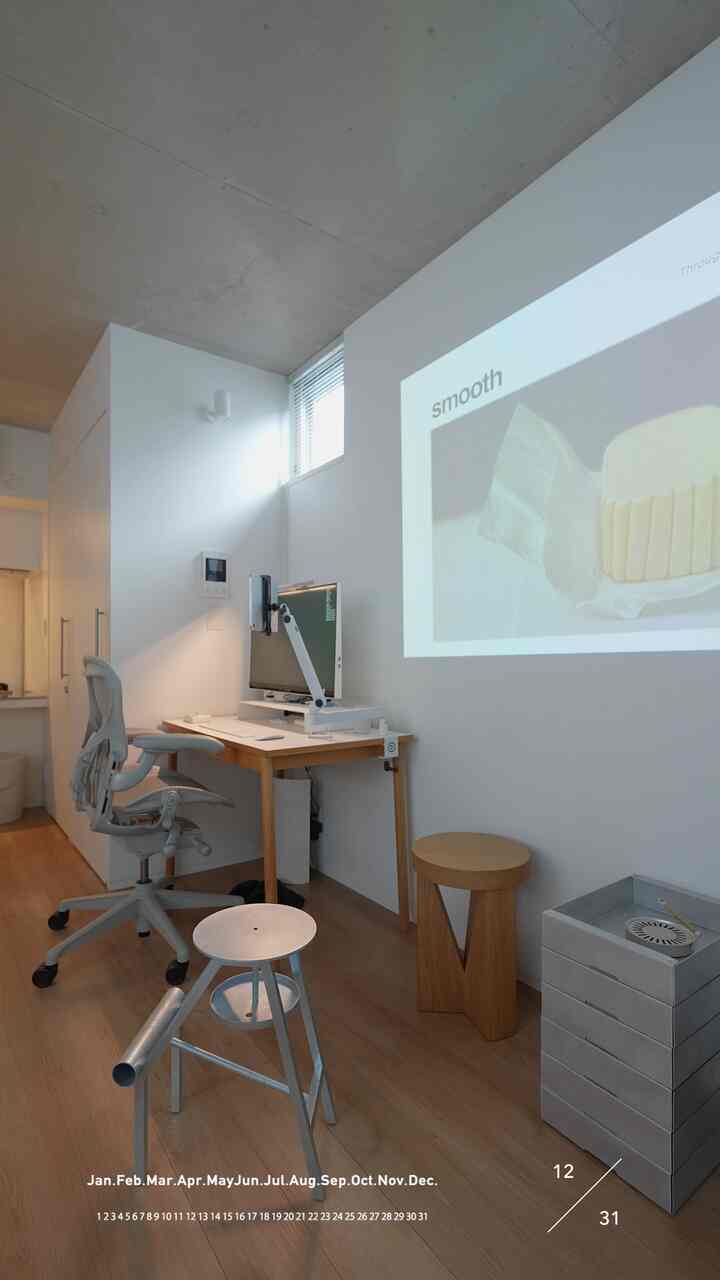 A white and wood-toned small studio apartment home office featuring a simple desk and office chair with a minimalistic interior