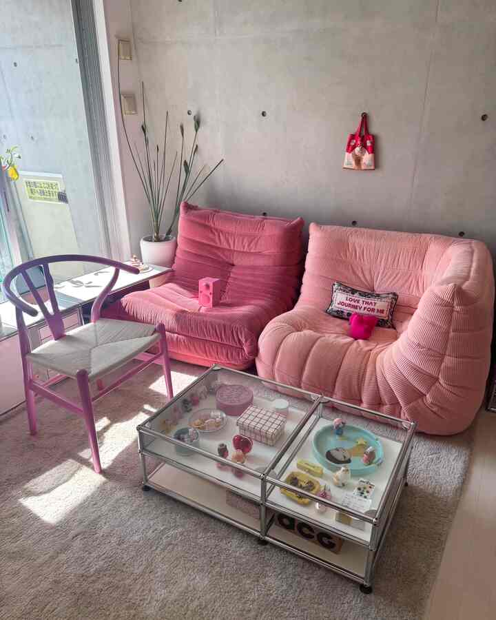 ピンク色調のリビングルーム、ピンクのセクショナルソファ、紫のYチェア、ガラステーブルが配置された印象的な空間