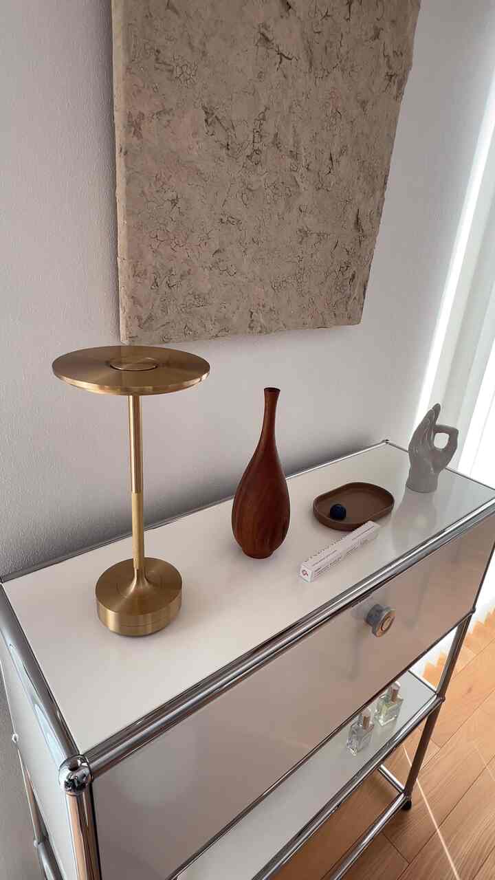 白とゴールドのトーンのサイドボードにテーブルランプと木製花瓶が配置されたシンプルなインテリア