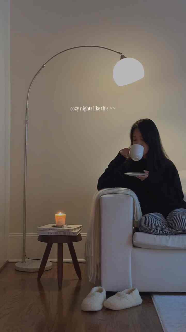 Natural warm-toned living room featuring a white sofa, floor lamp, and a lit candle on a stool creating a cozy ambient lighting