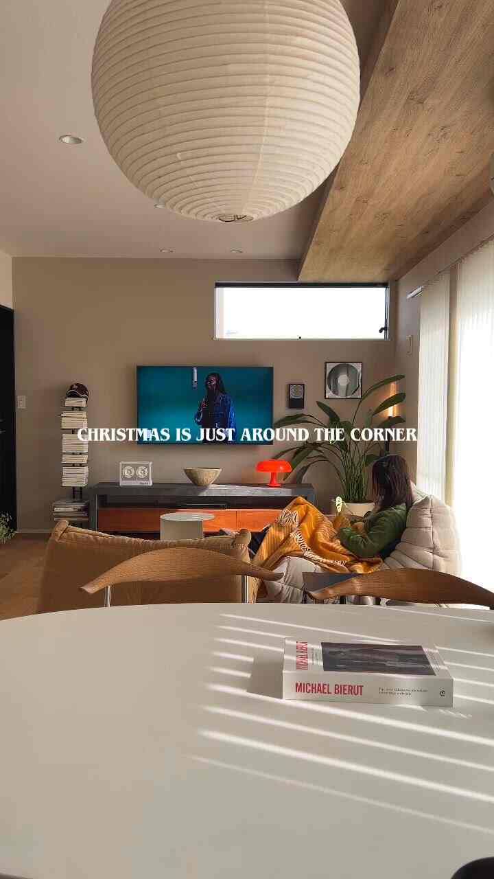 A bright living room with white and natural wood tones featuring a sofa, TV, and an orange floor lamp creating a cozy atmosphere