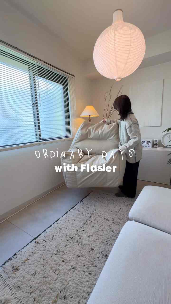 白とナチュラルカラーのリビング、中央にクリーム色のビーズクッションソファと大きなペンダントライトが配置された雰囲気のある空間