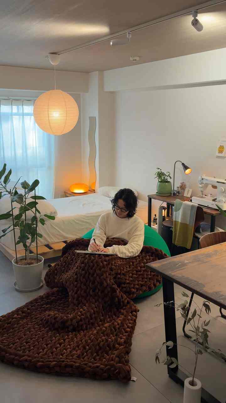 ナチュラルな色調のワンルーム寝室、白い壁と木製家具、茶色のスローと植物が配置された落ち着いた雰囲気のインテリア