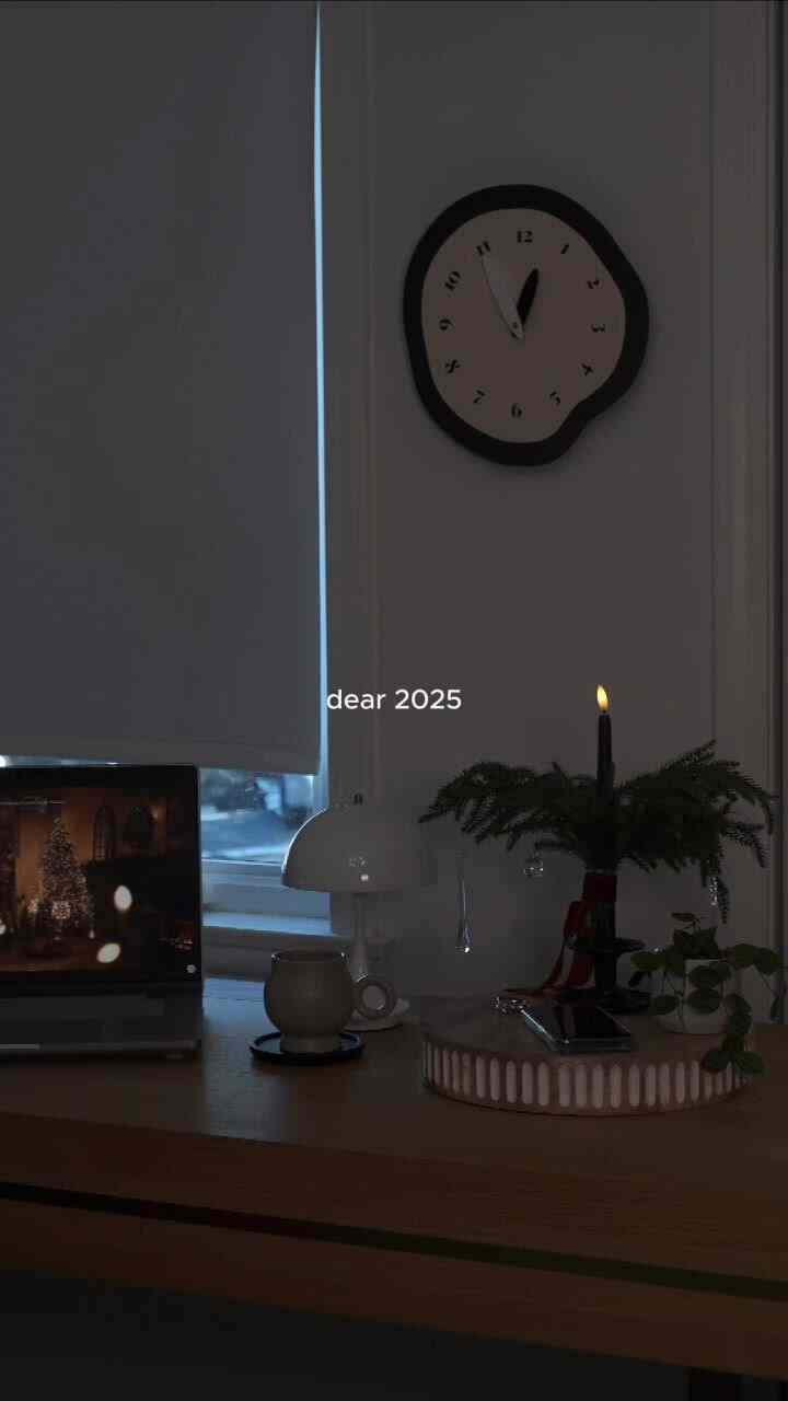 Modern home office with white walls and wood-toned desk, featuring a clock, candle, and plants creating a cozy atmosphere