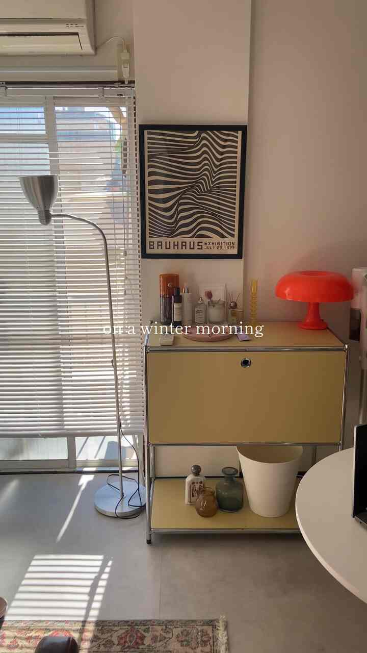 ベージュトーンの一人暮らしリビング、ミッドセンチュリーモダンの収納と赤いテーブルランプが配置された印象的な空間